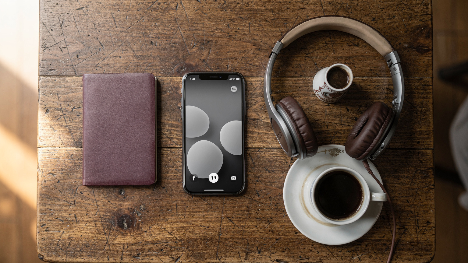 An overhead flat-lay of a minimalist travel setup: a passport, a smartphone with a Cellesim eSIM logo visible, a pair of worn travel headphones, and a small, locally-branded coffee cup on a hostel common area table.