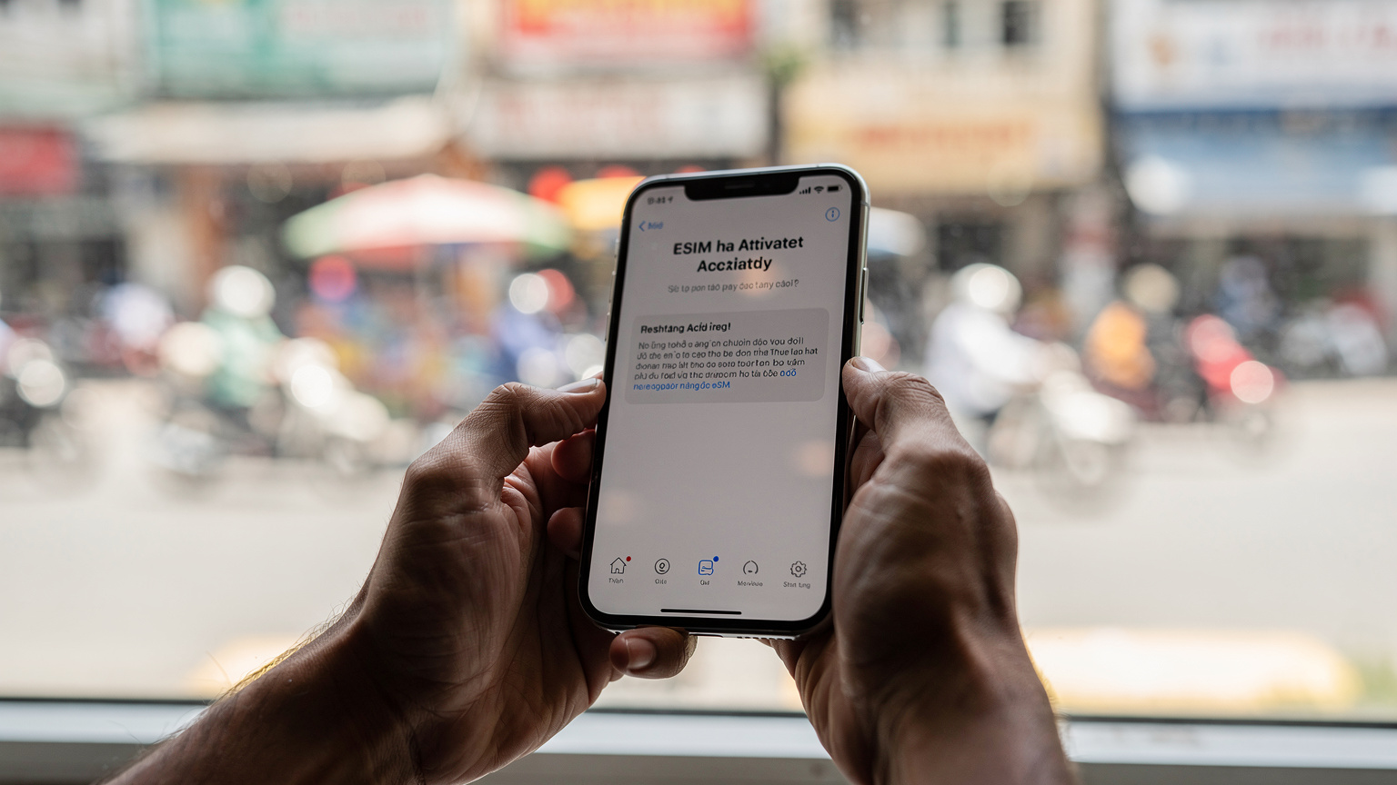 Eine Nahaufnahme eines Smartphones, das eine Meldung über eine erfolgreiche eSIM-Aktivierung anzeigt, gehalten von Händen vor einem Fenster mit Blick auf eine geschäftige Straße in Ho-Chi-Minh-Stadt.