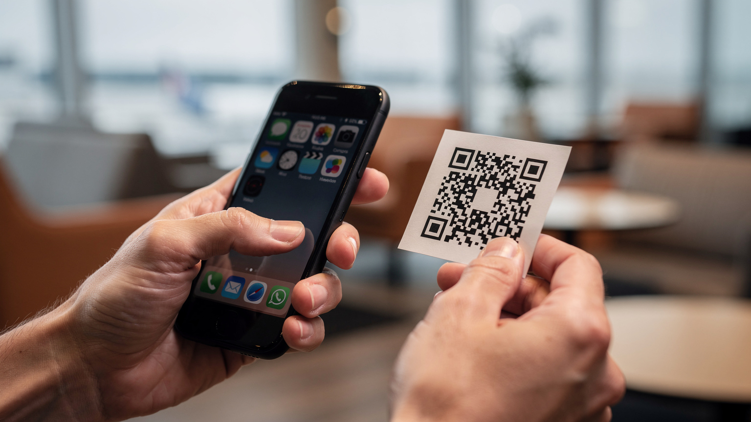 A close-up of hands holding a smartphone, scanning a QR code for eSIM activation with a blurred airport lounge in the background.