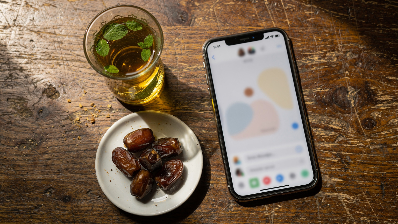 A close-up of a phone screen showing a messaging app interface, with a traditional Algerian tea glass and dates in the background, illustrating digital communication during travel.