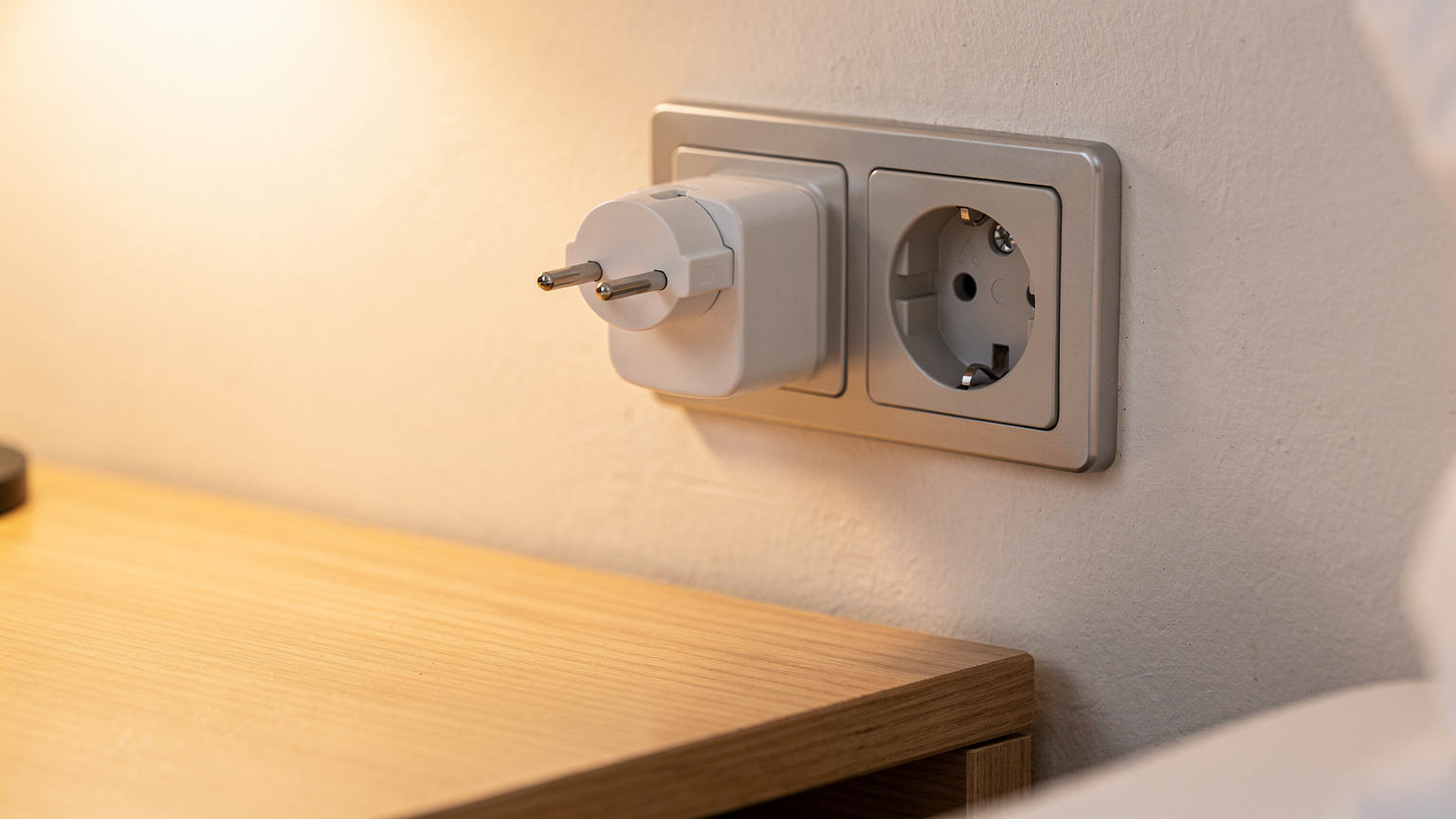 O ilustrație a unei prize de tip J cu un adaptor de priză universal conectat, pe o masă de lemn într-o cameră de hotel modernă din Zurich.