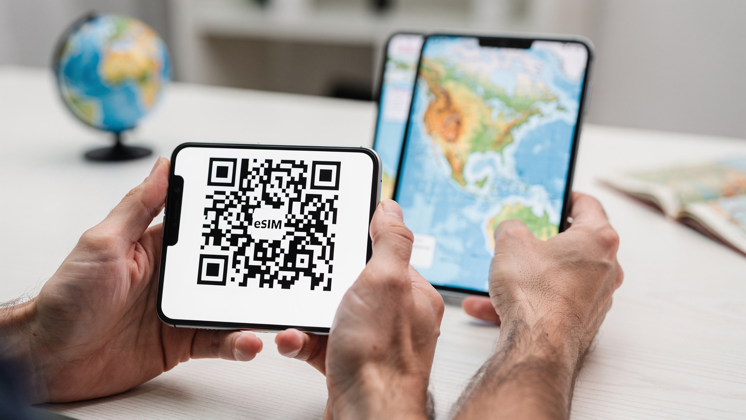 Close-up of hands holding a smartphone displaying an eSIM activation QR code on the screen, with a digital map of North America in the background.