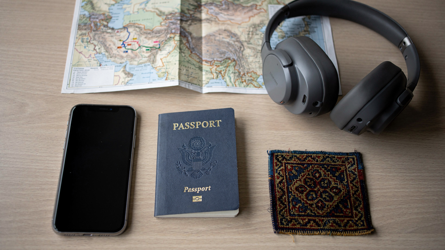 An overhead flat-lay of a digital nomad's organized desk with a passport, a smartphone, noise-canceling headphones, and a detailed paper map of Central Asia.