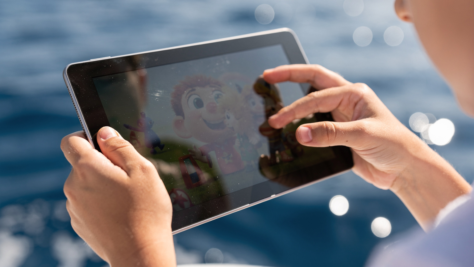 Närbild på ett barns händer som håller en surfplatta med en nedladdad film från Disney+, med det glittrande Egeiska havet i bakgrunden. Fokus ligger på interaktionen med surfplattan och barnets händer.
