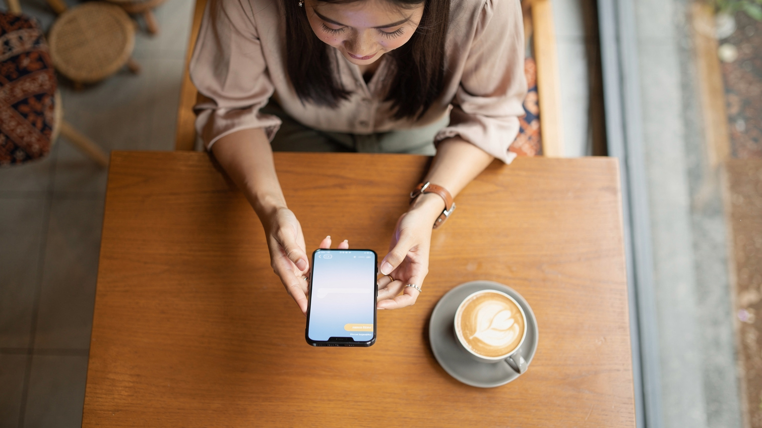 Seorang wanita muda sedang membandingkan paket-paket eSIM di ponselnya di sebuah kafe modern di daerah Kebayoran Baru, Jakarta, dengan secangkir kopi di sampingnya, mempersiapkan diri untuk perjalanan.