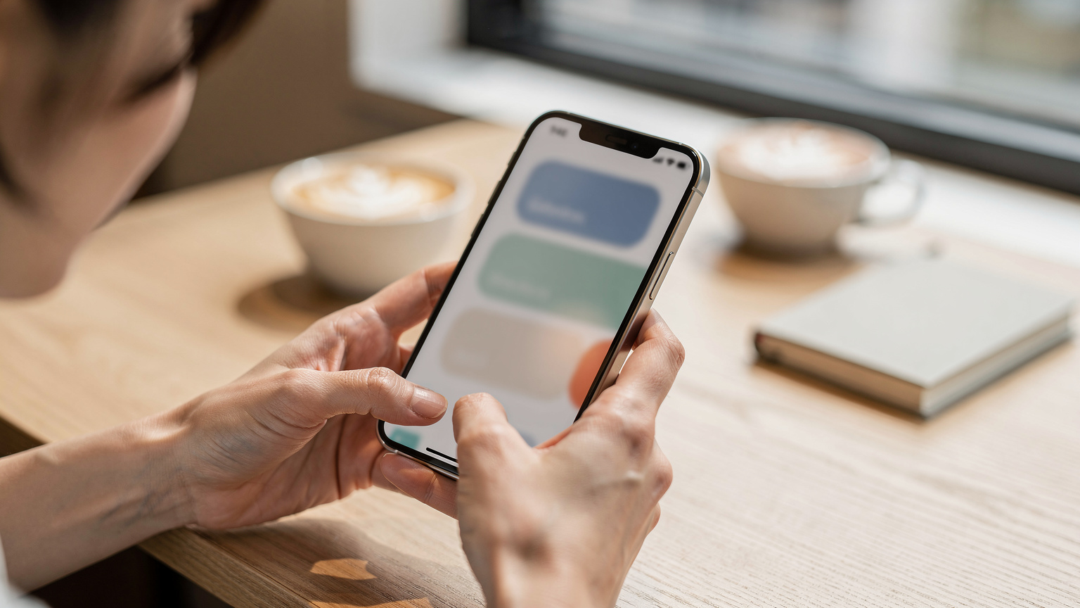 カフェのテーブルでiPhoneを使ってCellesimのウェブサイトでeSIMプランを検索し、購入手続きを進めている日本人女性の手元。
