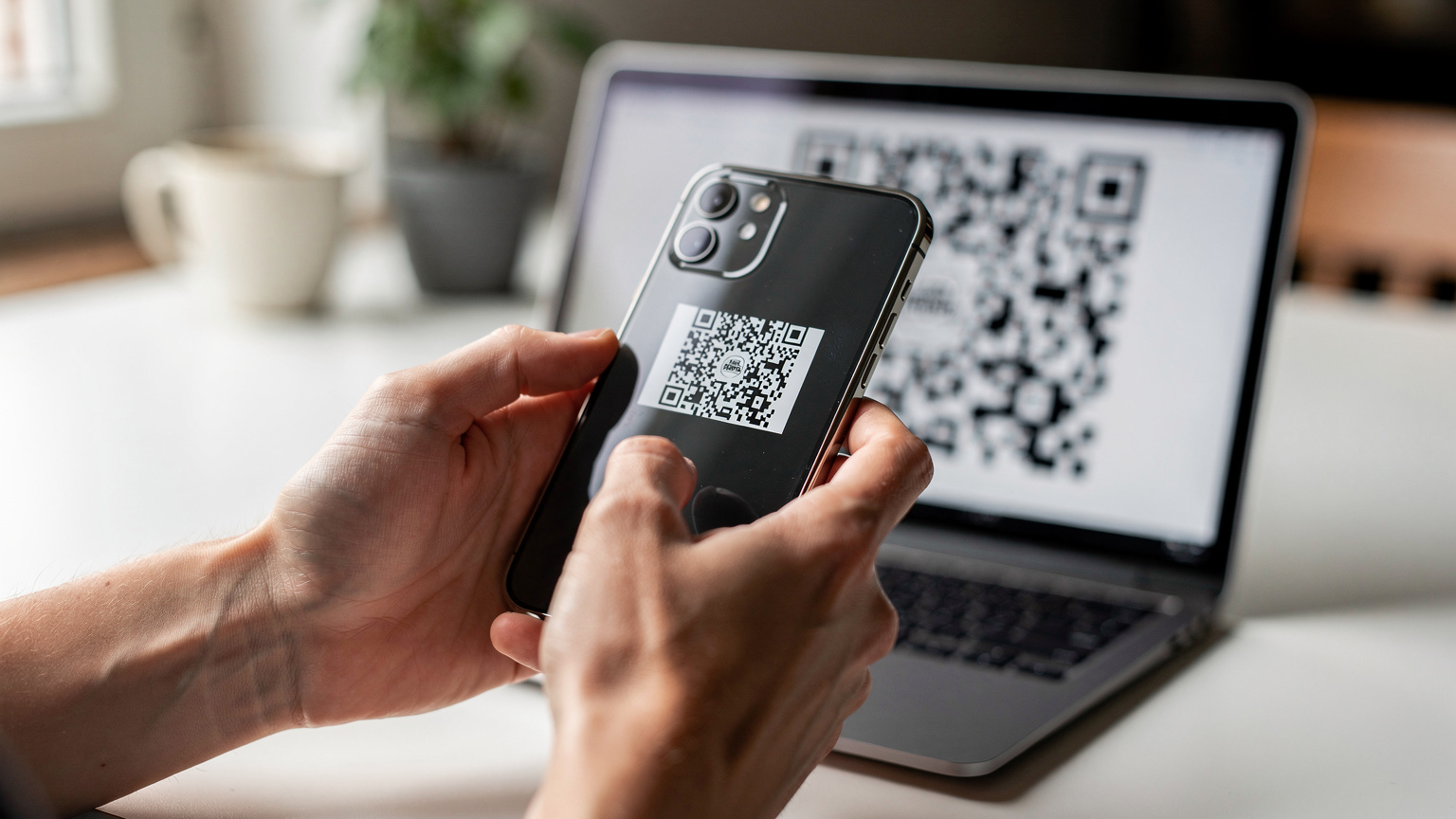 Close-up van handen die een iPhone vasthouden en een QR-code scannen op een computerscherm, wat de eenvoud van eSIM-activering illustreert.