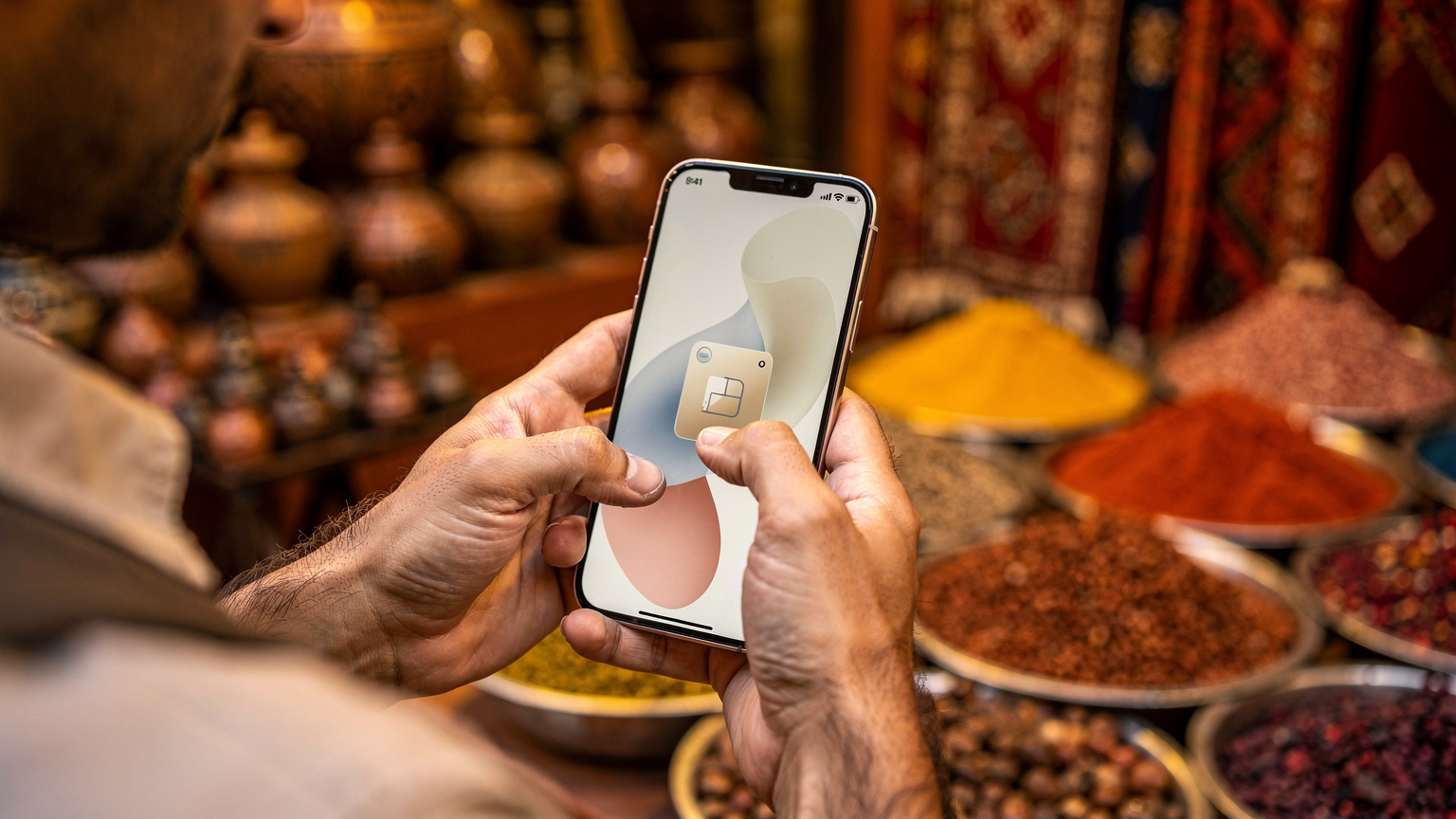 Руки путешественника используют смартфон для активации eSIM, на заднем плане смутно виден египетский рынок с местными специями.