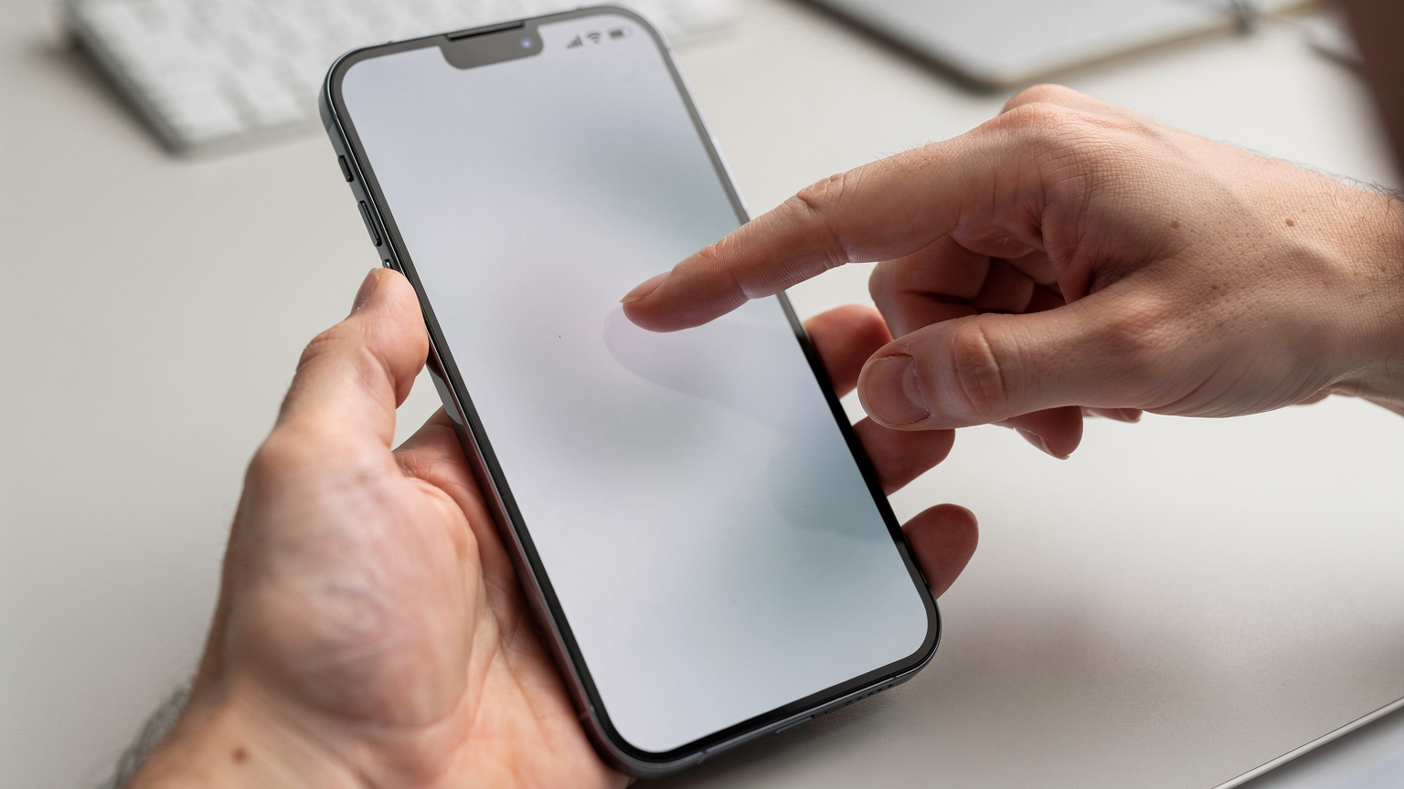A person's hands holding a smartphone, displaying the phone's settings screen with blurred text, while another hand points to a section of the screen, indicating a precise interaction.