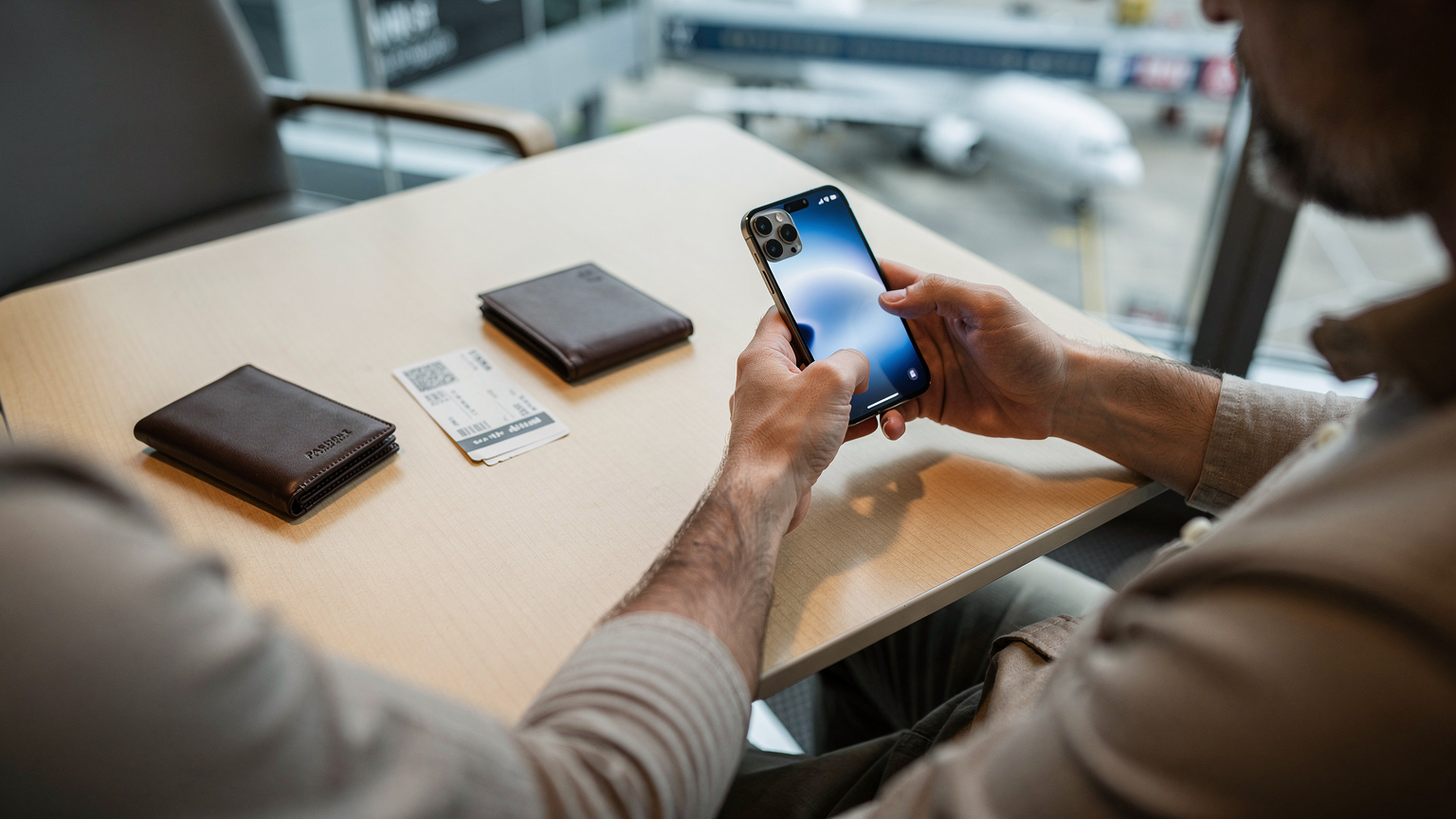 Un voyageur à l'aéroport consulte son iPhone 14, un modèle américain sans tiroir SIM physique, activant son plan eSIM avant l'embarquement.