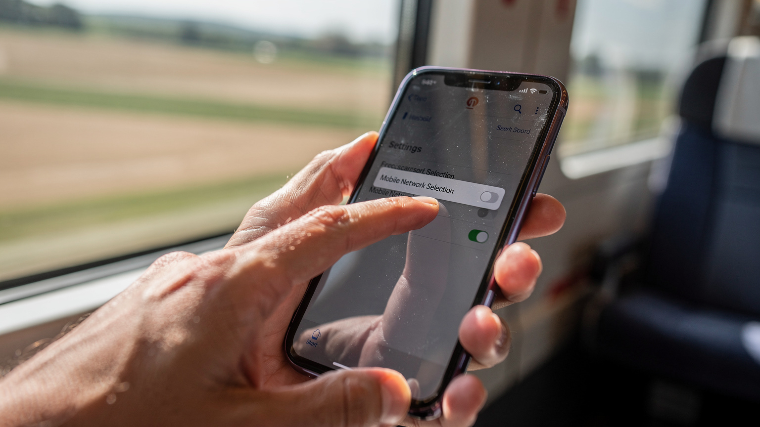Un primo piano su un dito che seleziona un'opzione di rete mobile in un'app di impostazioni su uno smartphone, con un treno ad alta velocità italiano sullo sfondo sfocato, indicando la necessità di connettività in movimento.