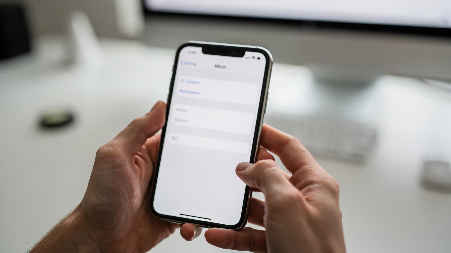 Prim-plan pe mâinile unei persoane care ține un iPhone deschis la ecranul de setări, cu secțiunea 'Despre' evidențiată, arătând câmpul 'EID'.