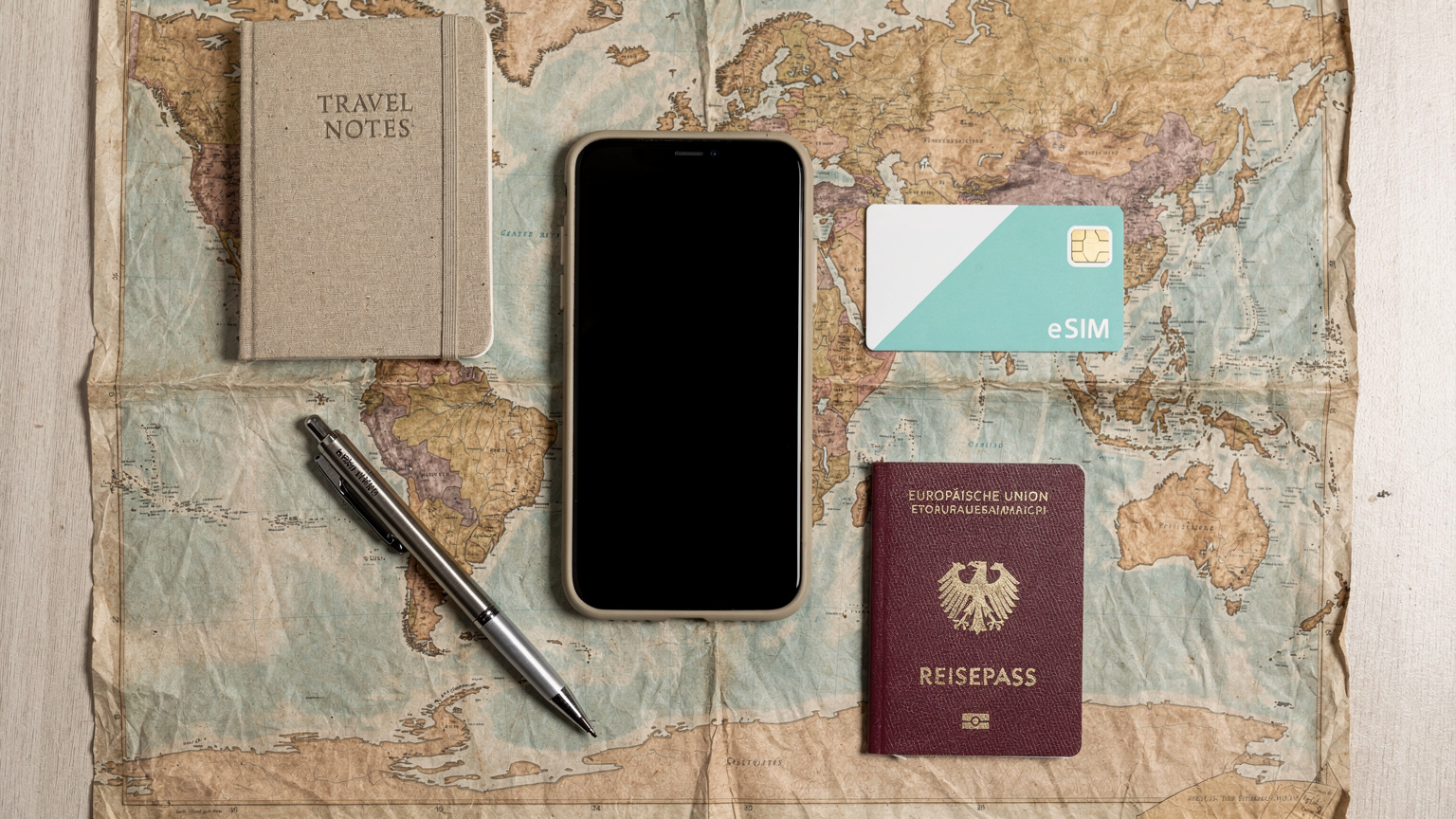 Ein Smartphone liegt auf einer verknitterten Weltkarte. Daneben liegen eine Cellesim-Verpackung, ein Kugelschreiber und ein Reisepass, alles bereit für die nächste Reiseplanung.