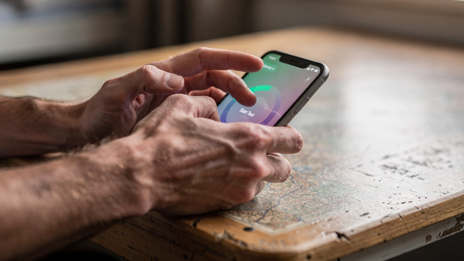 Eine Nahaufnahme zeigt die Hände einer Person, die auf einem Smartphone eine Speedtest-App bedient, während die Anzeige sich aufbaut. Der Fokus liegt auf der Interaktion.