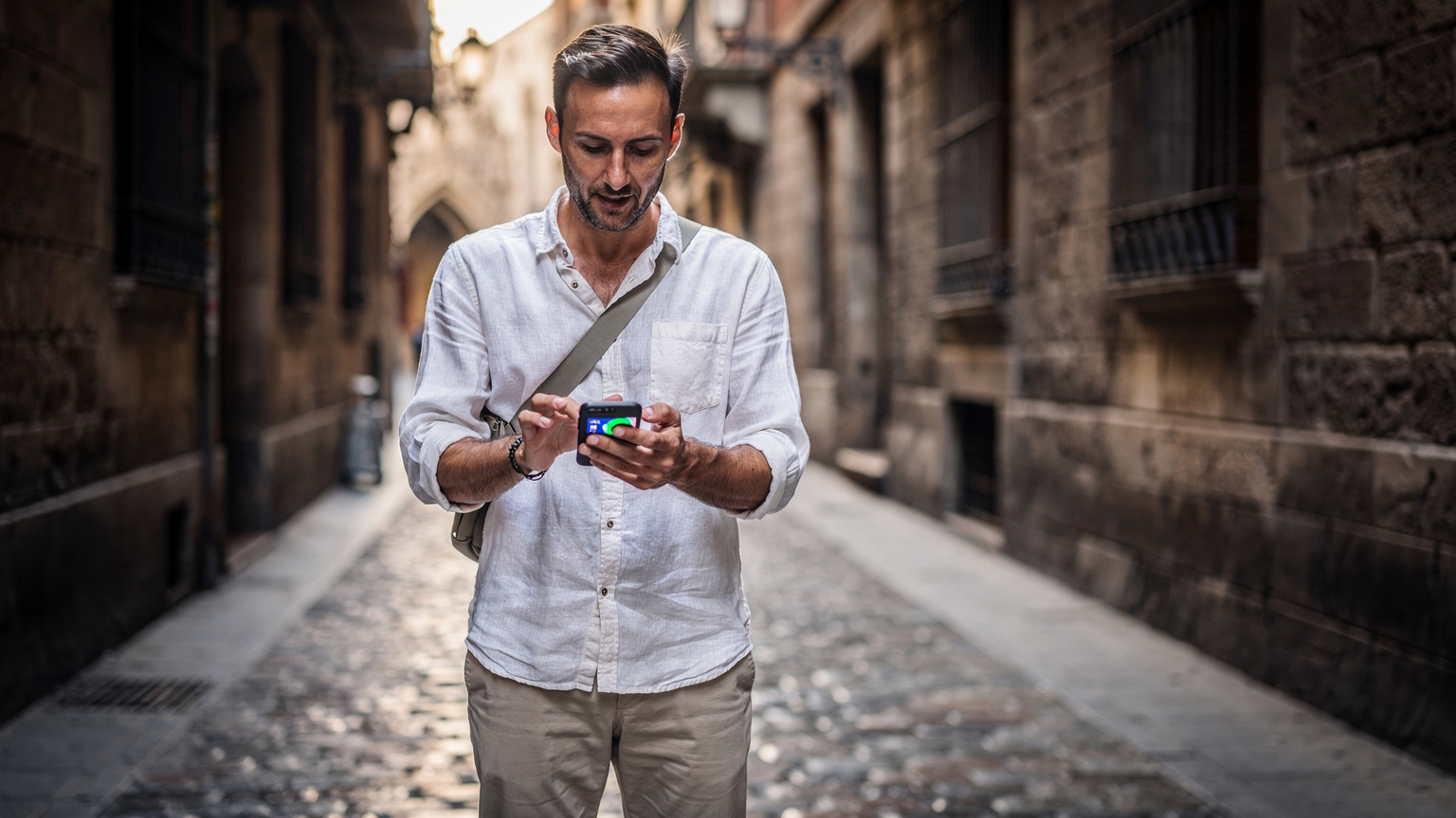 Un viajero en el barrio Gótico de Barcelona, concentrado en su teléfono mientras realiza un test de velocidad, con las antiguas fachadas de piedra como telón de fondo.