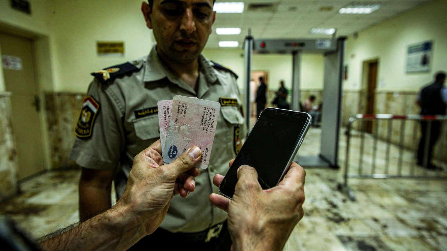 Une personne montre son passeport et son téléphone à un agent de sécurité à l'entrée d'un bureau de poste égyptien typique, soulignant le besoin d'identification pour certains services.