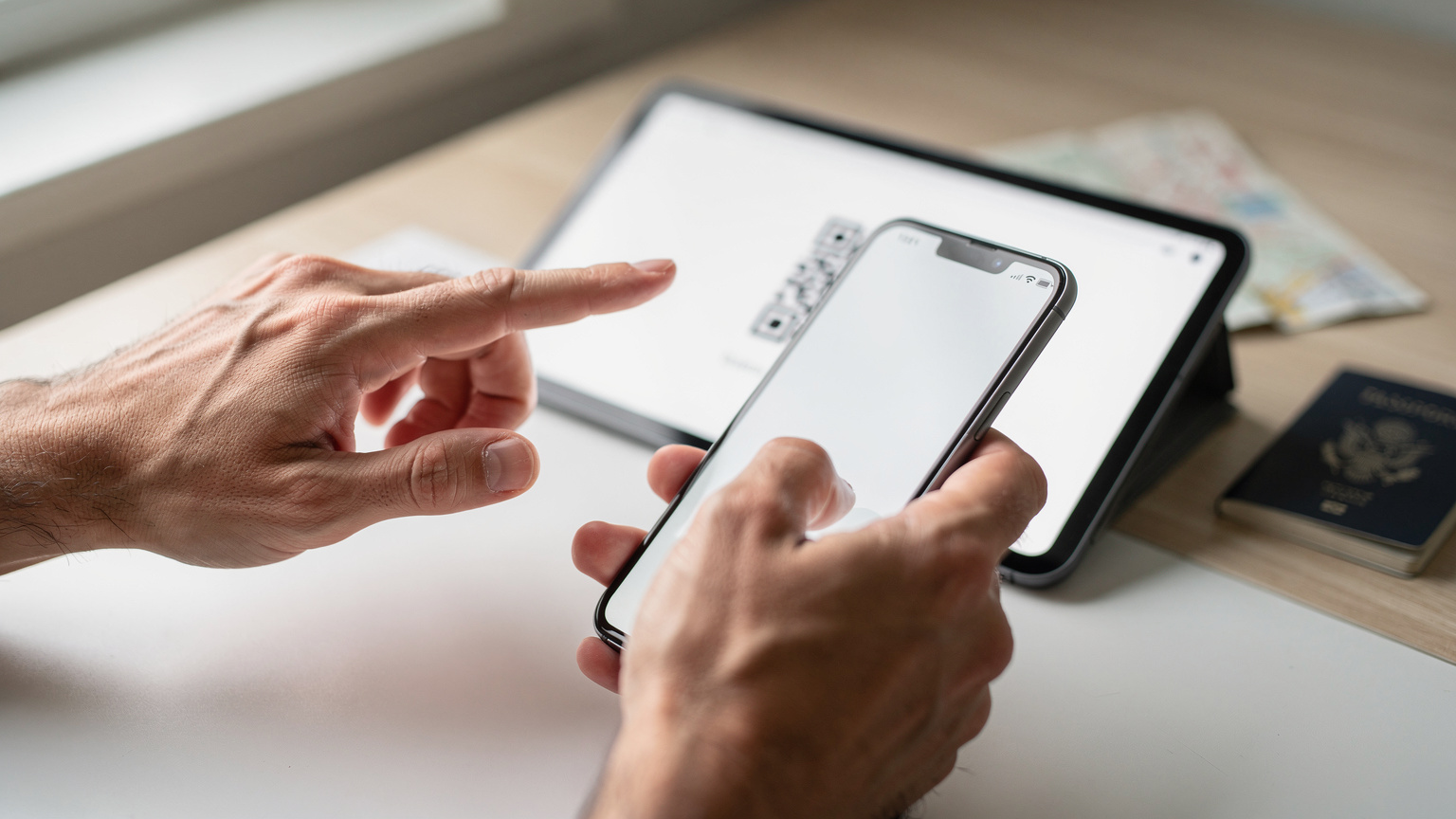 Κοντινό πλάνο σε χέρια που κρατούν ένα smartphone, με έναν QR κωδικό eSIM να εμφανίζεται στην οθόνη ενός tablet στο παρασκήνιο, έτοιμο για σάρωση.