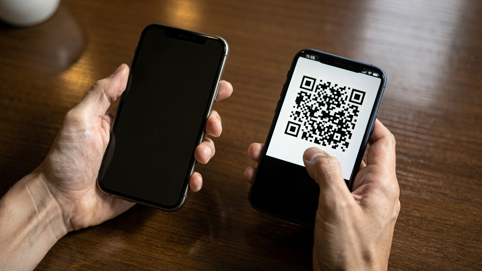 カフェのテーブルで、旅行者の手がiPhone 18の画面を操作し、eSIMのQRコードをスキャンしているクローズアップ。指先が画面に触れる瞬間を捉え、デバイスとユーザーのインタラクションを強調。