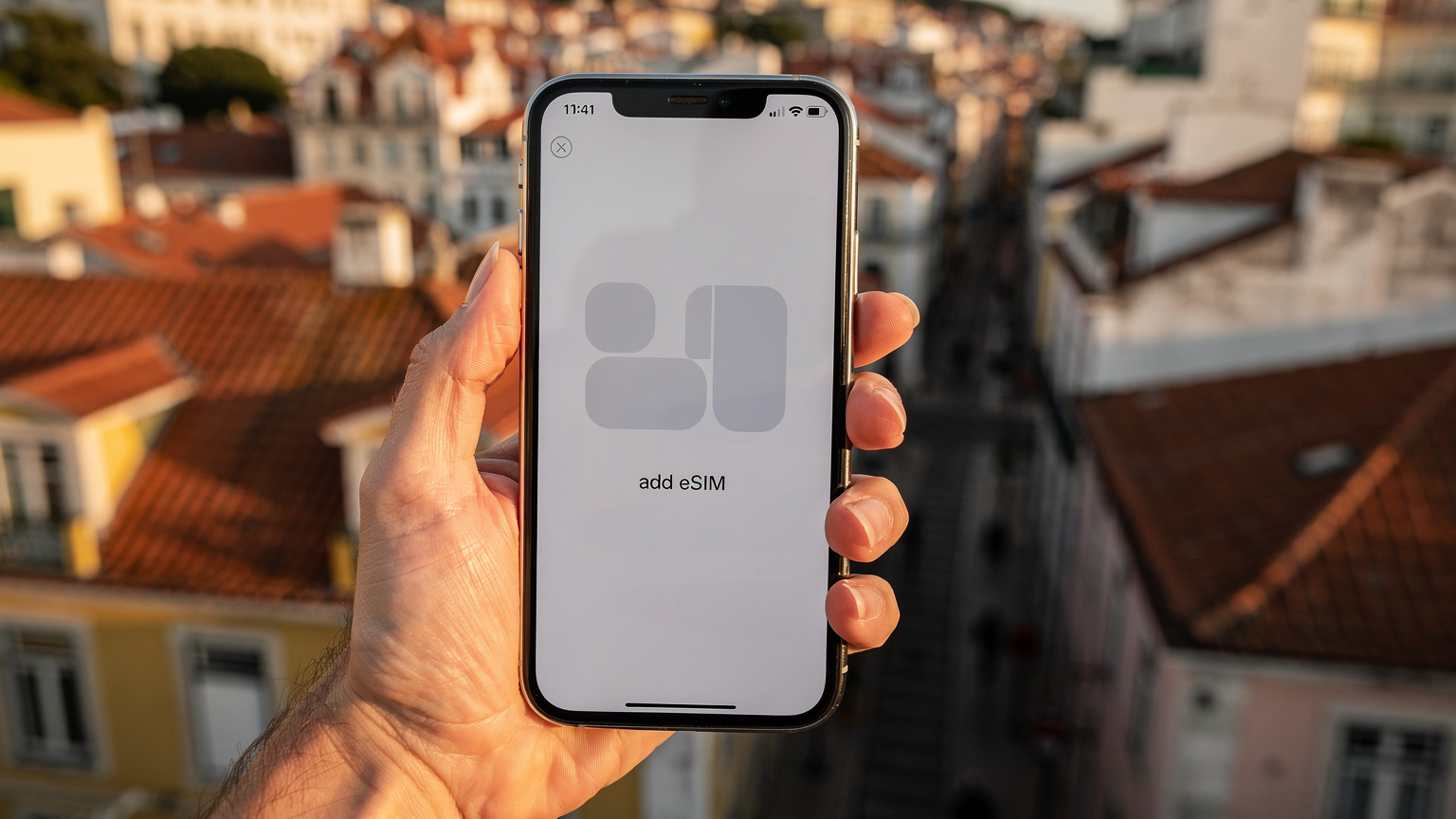 Een close-up van een hand die een smartphone vasthoudt met een eSIM-activatie-scherm, tegen de achtergrond van een zonnig Europees stadsgezicht.