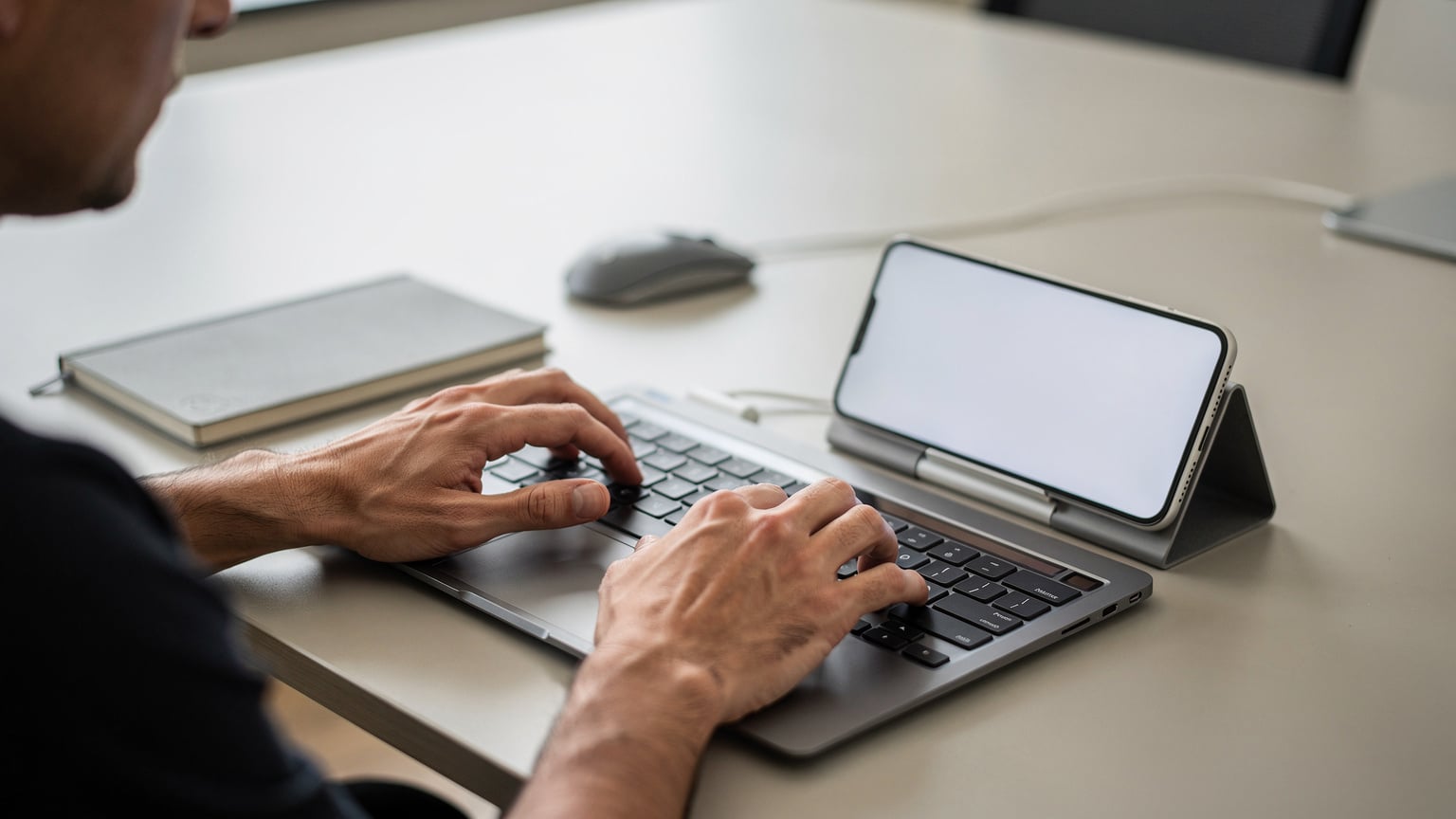 A close-up of hands typing on a laptop keyboard, with a smartphone open to a customer support chat interface resting beside it, indicating a troubleshooting scenario.