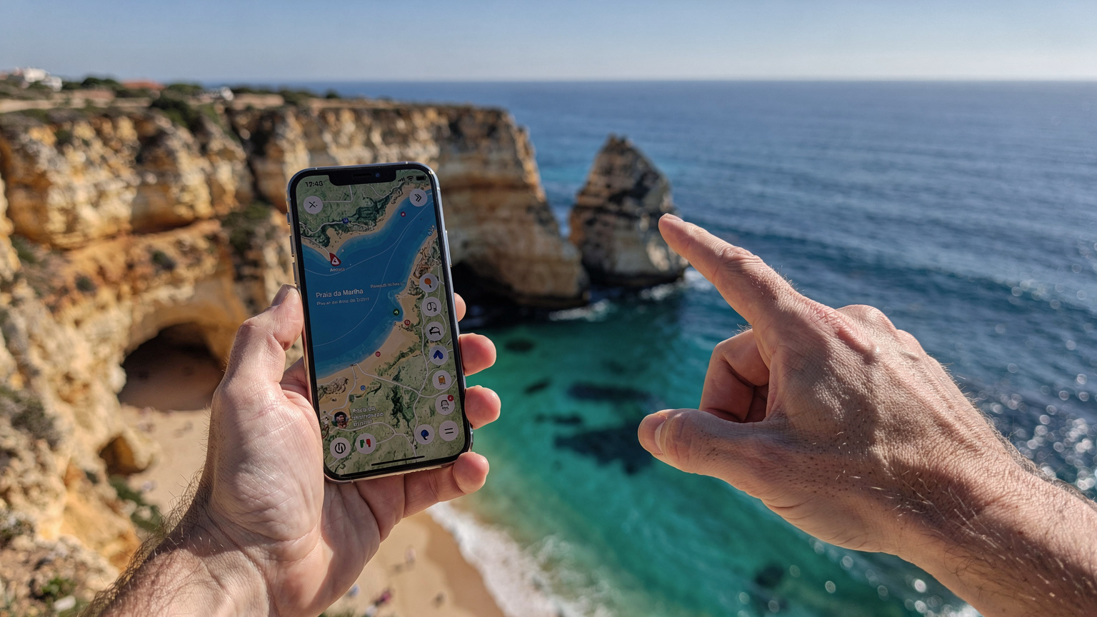Uma mão segura um iPhone 18 exibindo um mapa da Praia da Marinha no Algarve, enquanto a outra mão aponta para o horizonte, revelando o oceano azul turquesa e falésias dramáticas sob um céu claro.