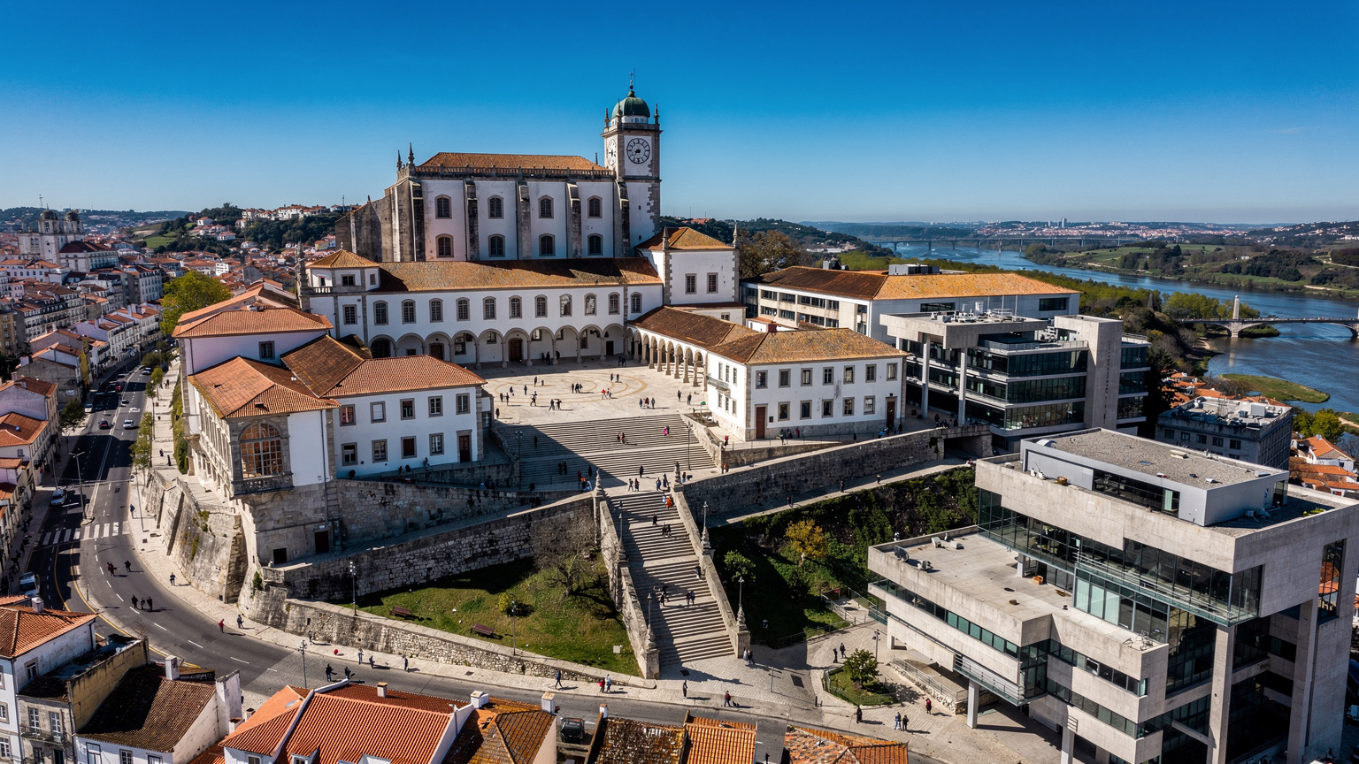 Uma vista aérea de um campus universitário em Coimbra, Portugal, com estudantes a circular entre edifícios históricos e modernos, simbolizando a mistura de tradição e tecnologia.