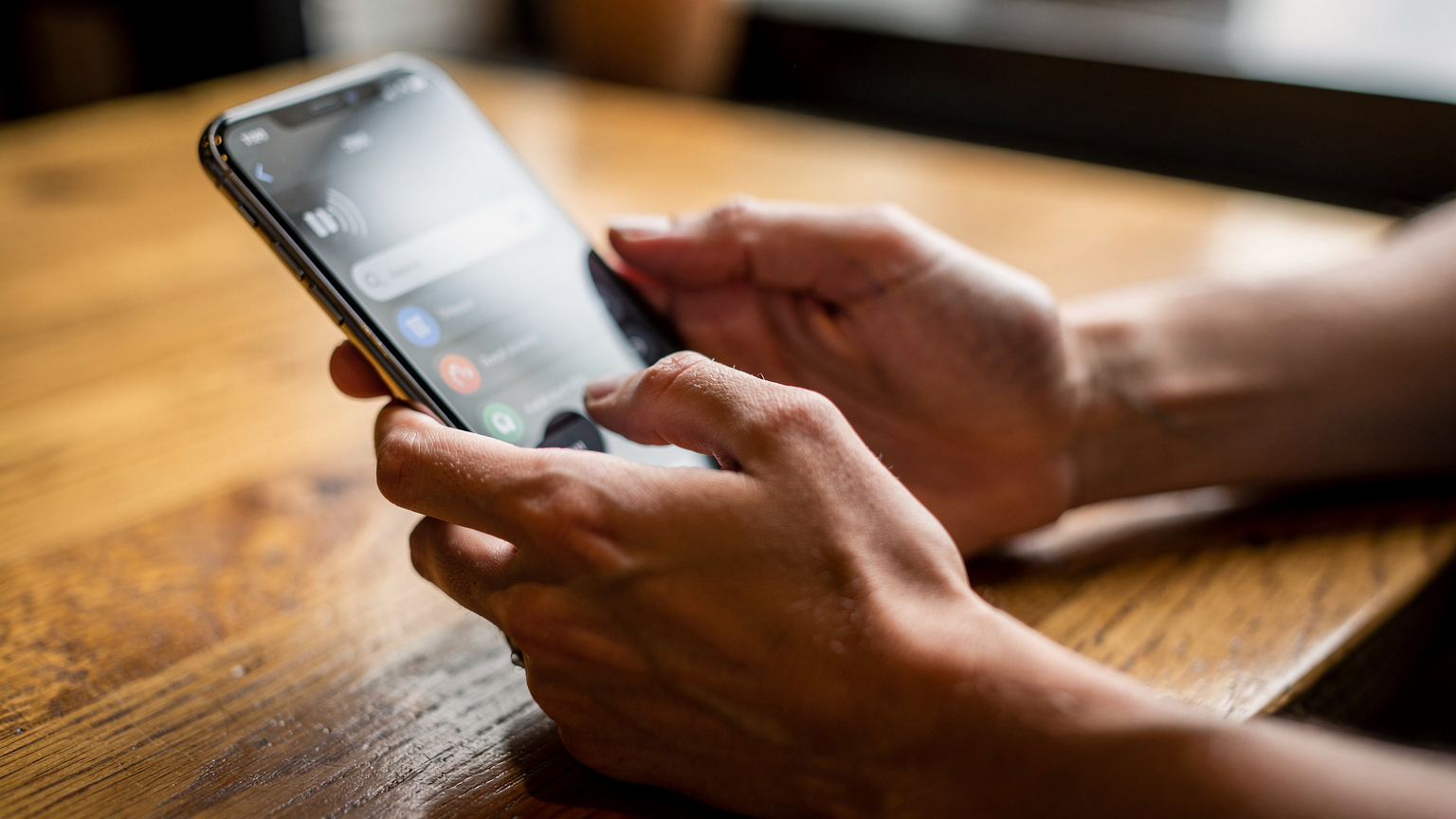 Tangan manusia memegang smartphone yang menampilkan layar pengaturan eSIM dengan ikon sinyal penuh, di atas meja kayu.