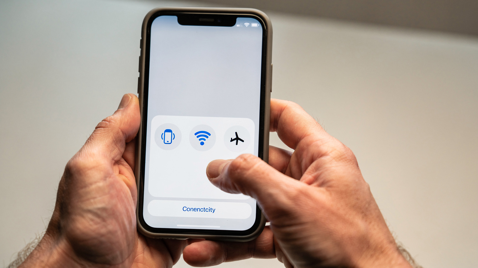 Primo piano sulle mani di una persona che tiene uno smartphone e scorre un menu di impostazioni, con icone che suggeriscono la gestione della connettività, in un ambiente neutro e moderno.