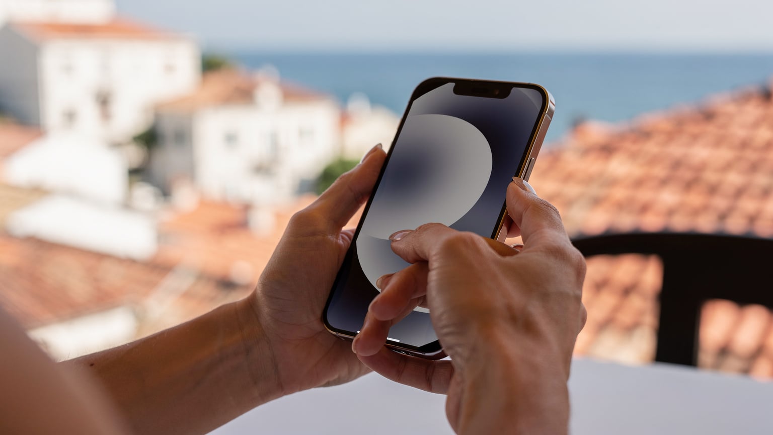 Жінка налаштовує eSIM на сучасному смартфоні, сидячи на терасі готелю з видом на Адріатичне море.