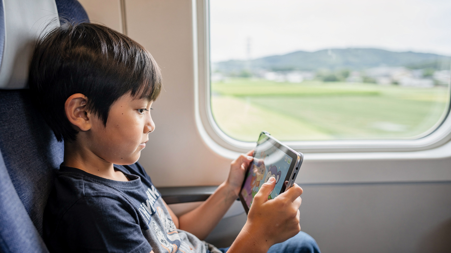 Ein Kind schaut während der Fahrt mit dem Shinkansen auf sein Tablet, während die japanische Landschaft vorbeizieht.