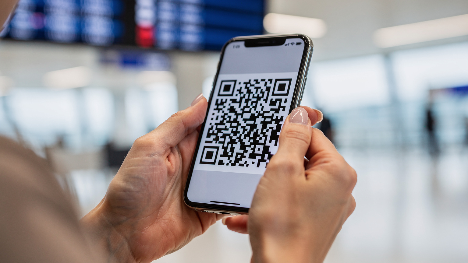 Крупний план, руки жінки тримають смартфон, на якому відкрито додаток з QR-кодом для активації eSIM, на тлі аеропорту.