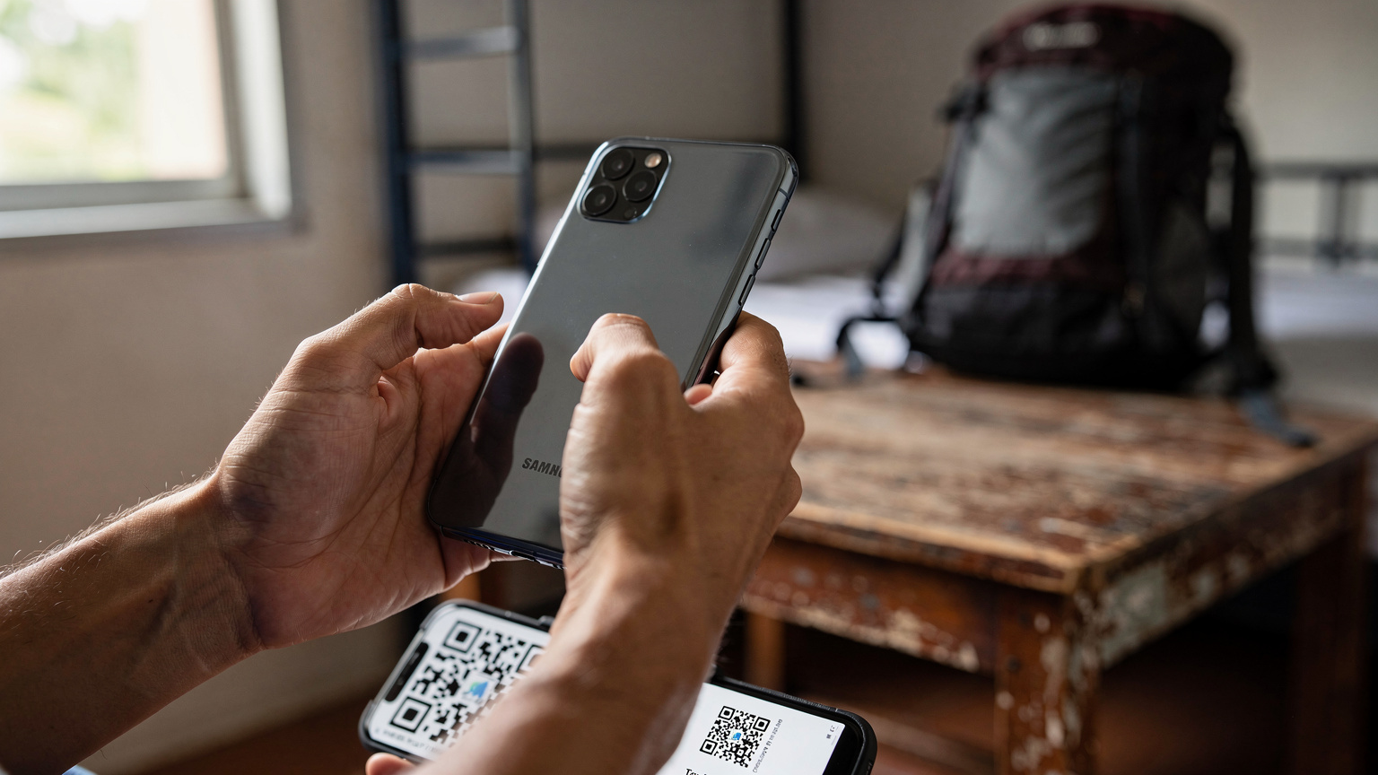 Een close-up van een paar handen die een smartphone vasthouden, gericht op het scannen van een QR-code voor eSIM-installatie, met op de achtergrond een onscherpe, maar herkenbare hostelkamer.