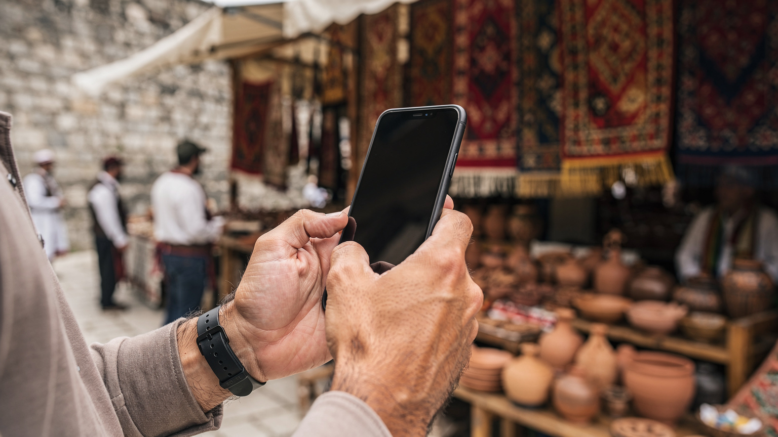 Bir gezginin elinde akıllı telefon ve Kosova'da yerel el sanatları pazarı.