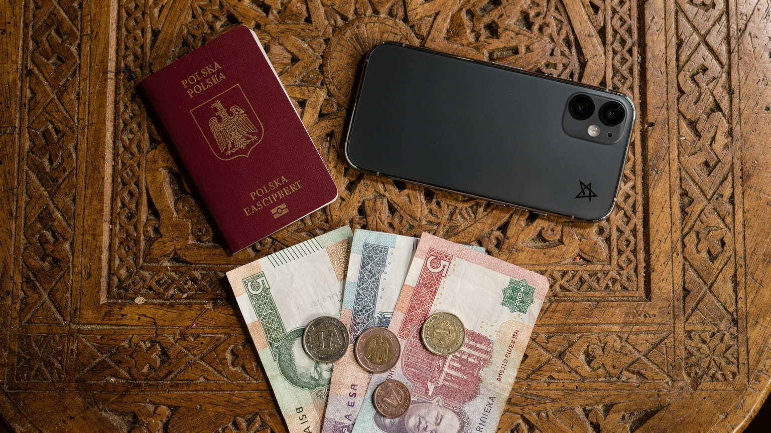 Zestaw podróżnika, w tym paszport, telefon z aktywowanym eSIM i marokańskie dirhamy, ułożone na drewnianym stole z tradycyjnym marokańskim wzorem.