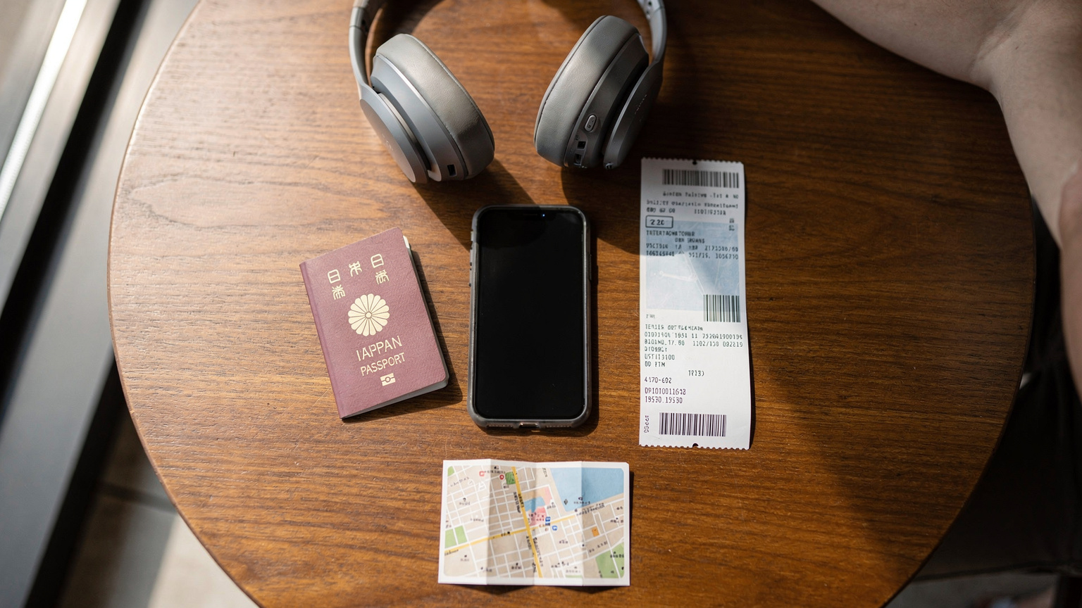 現代的なカフェのテーブルで、パスポート、飛行機の搭乗券、ヘッドフォンと一緒にiPhoneが置かれている。画面にはeSIM設定画面が表示されており、旅の準備が整っている雰囲気を表現。