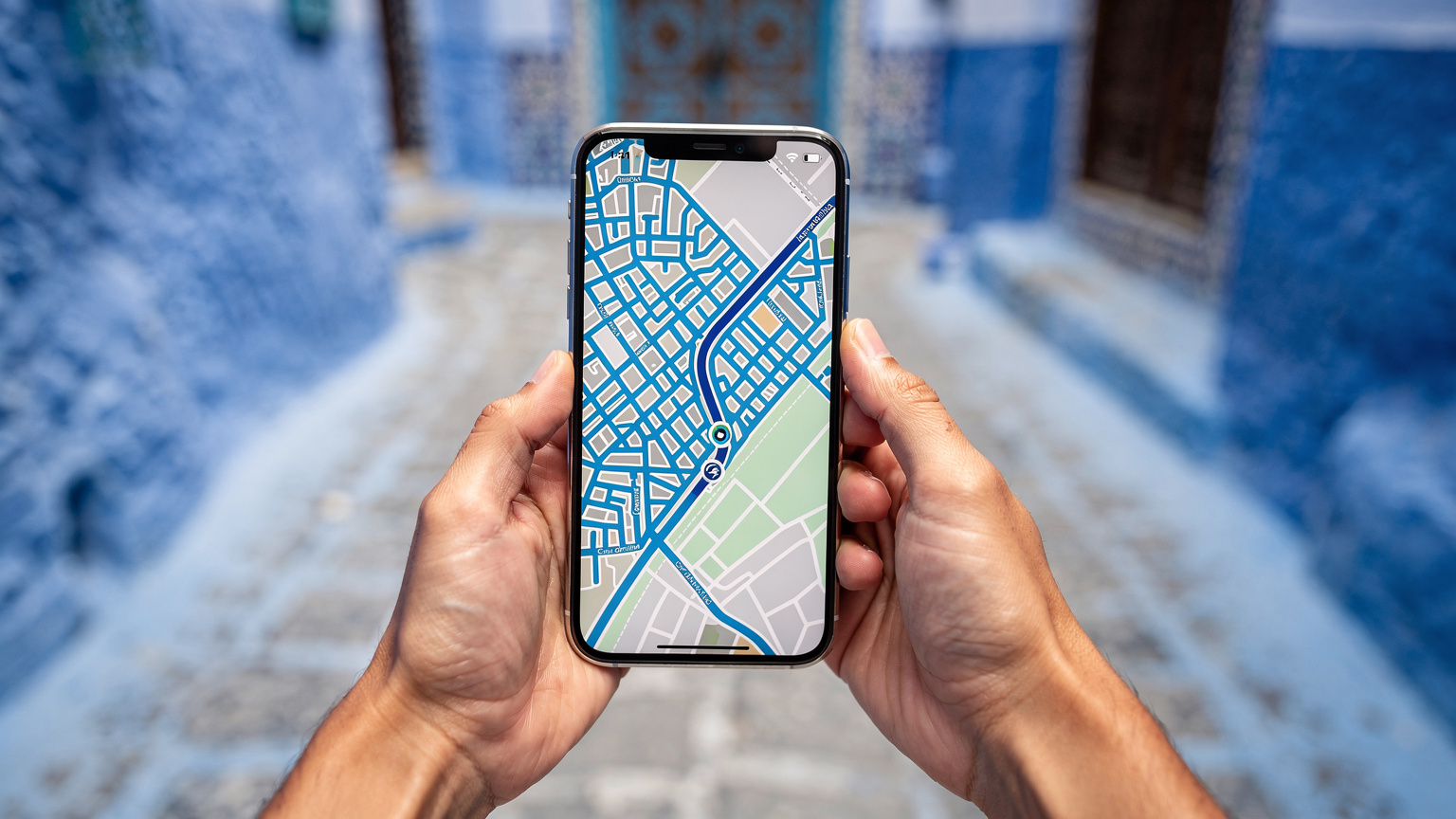 Ręce trzymające smartfon, na ekranie widać aplikację mapy z zaznaczoną trasą po błękitnych uliczkach Chefchaouen.