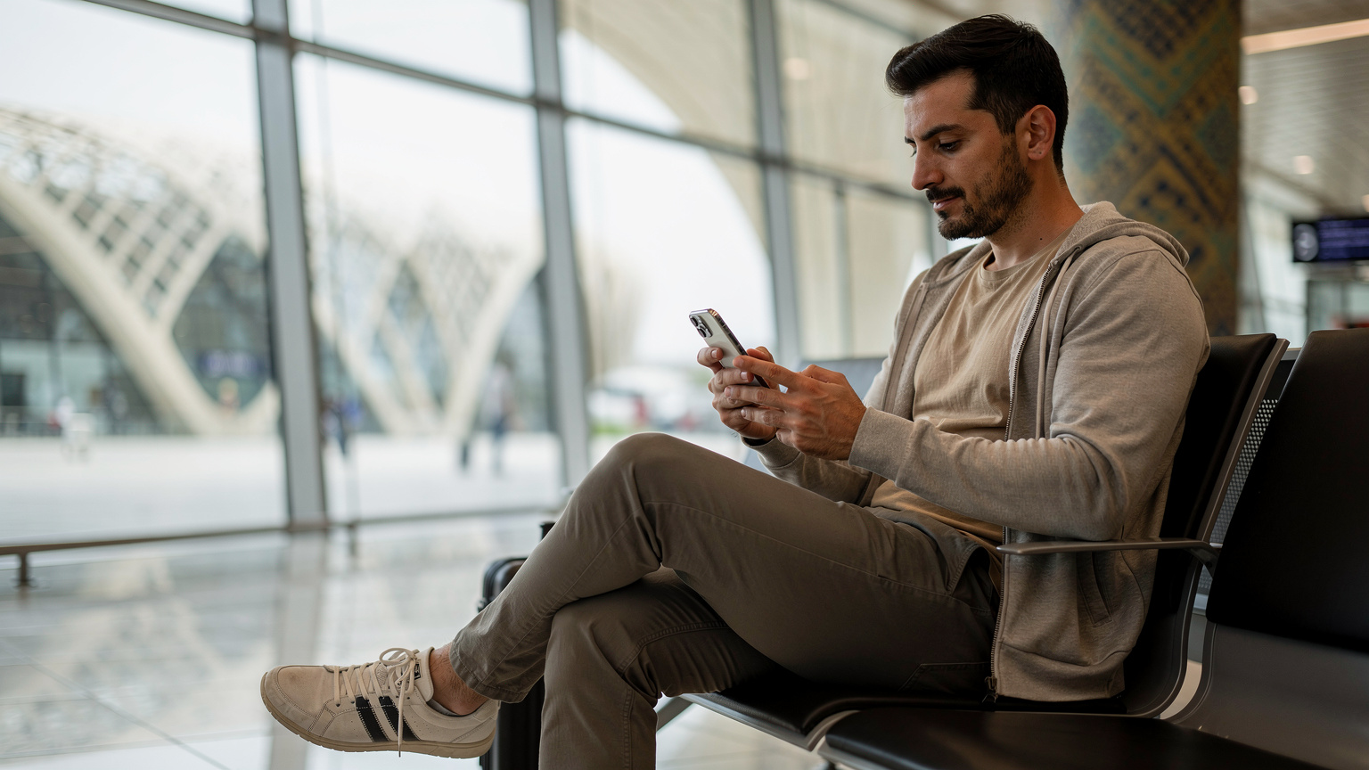 Ein Reisender entspannt sich auf einer Bank am Flughafen von Baku, Aserbaidschan, und aktiviert eine eSIM auf seinem Smartphone, um sofort nach der Landung online zu sein.