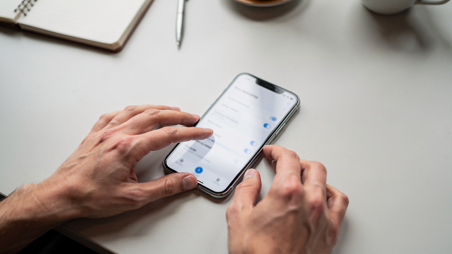 Un primo piano delle mani di una persona che naviga nelle impostazioni di rete mobile del suo smartphone, mostrando le opzioni per la SIM fisica e l'eSIM, su uno sfondo sfocato di una scrivania moderna in un caffè co-working.