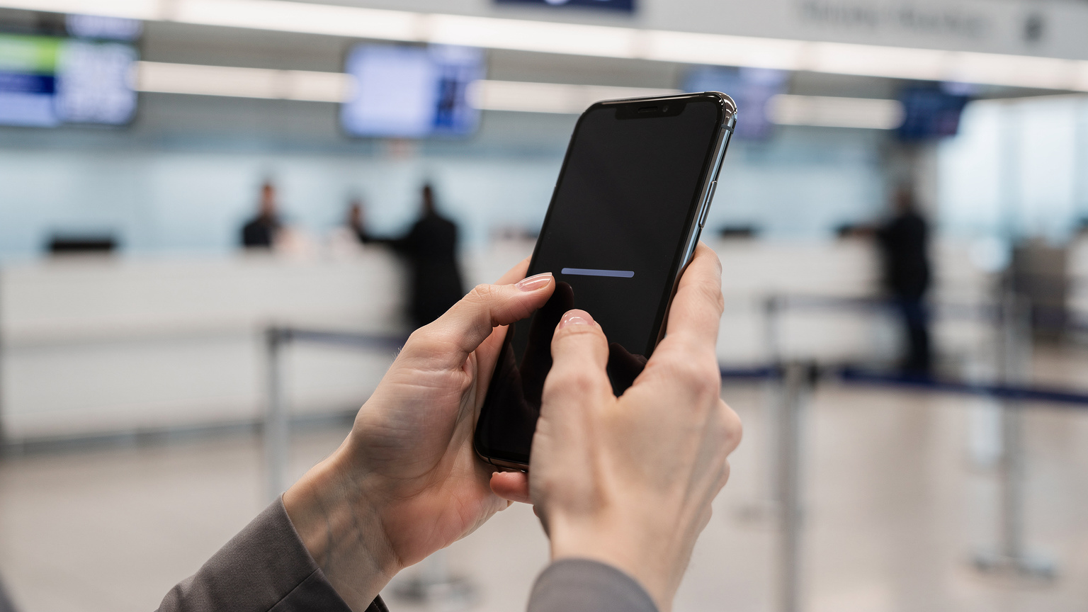 空港のチェックインカウンターを背景に、スマートフォンでeSIMのQRコードをスキャンしている女性の手元。