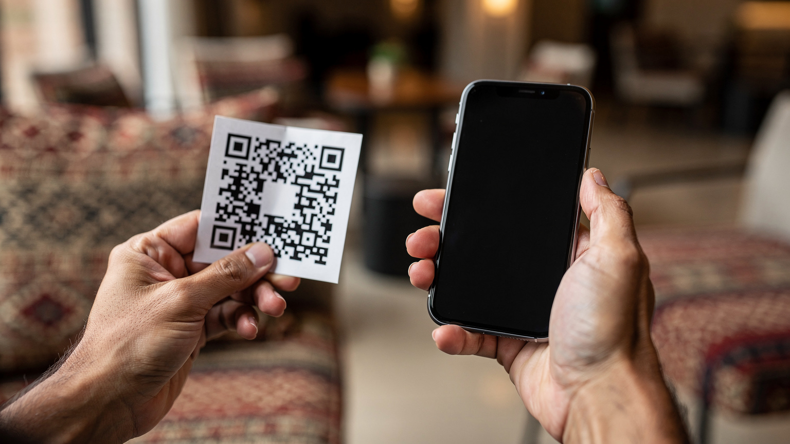 Un primer plano de manos sosteniendo un smartphone, mostrando el proceso de escaneo de un código QR para activar una eSIM, con un fondo ligeramente desenfocado de un hotel moderno en Cusco.