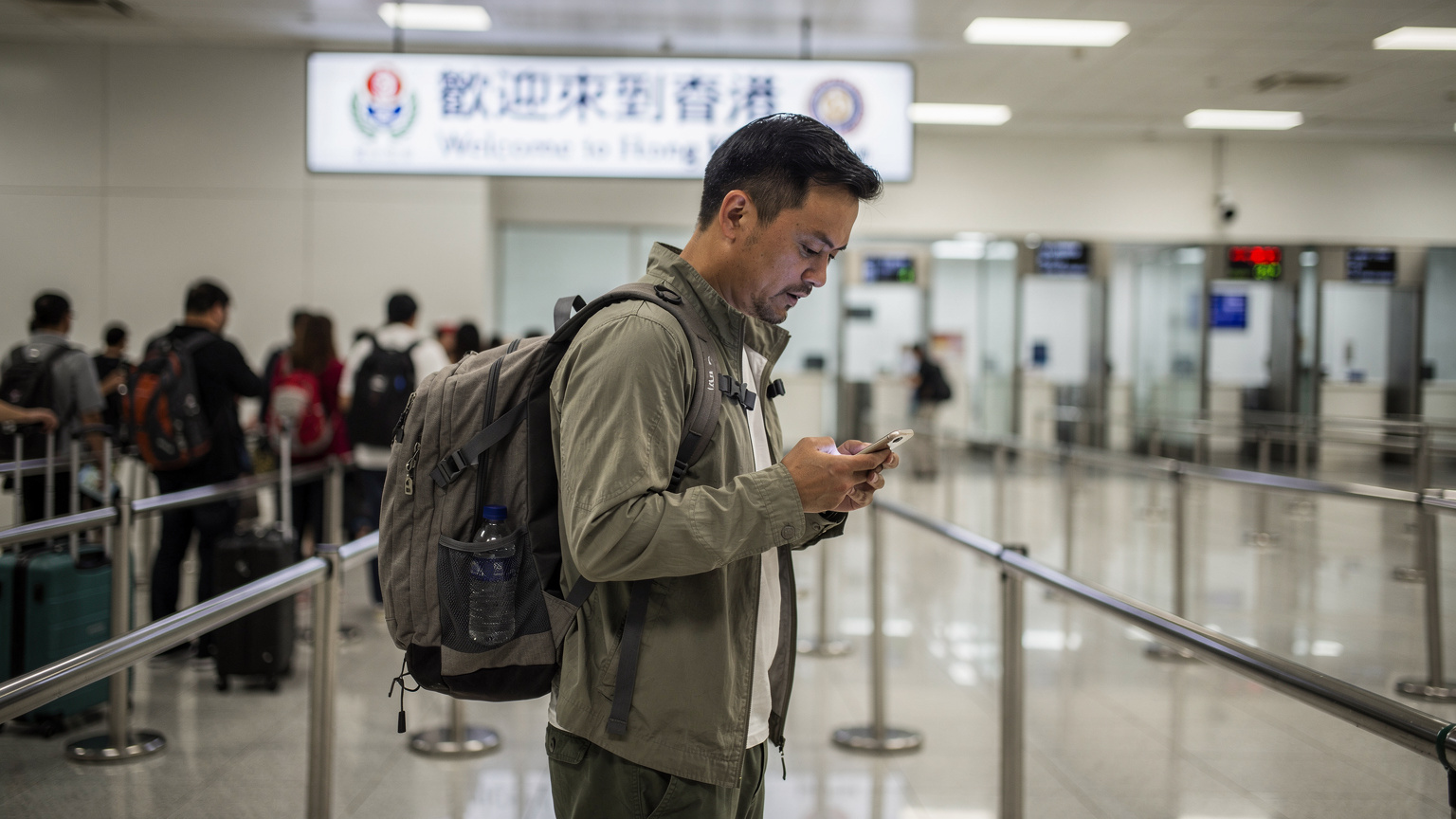 一位旅行者在深圳湾口岸的边检大厅里,焦虑地查看手机屏幕,周围是排队的人群和“欢迎来到香港”的指示牌,暗示着网络连接的困扰。