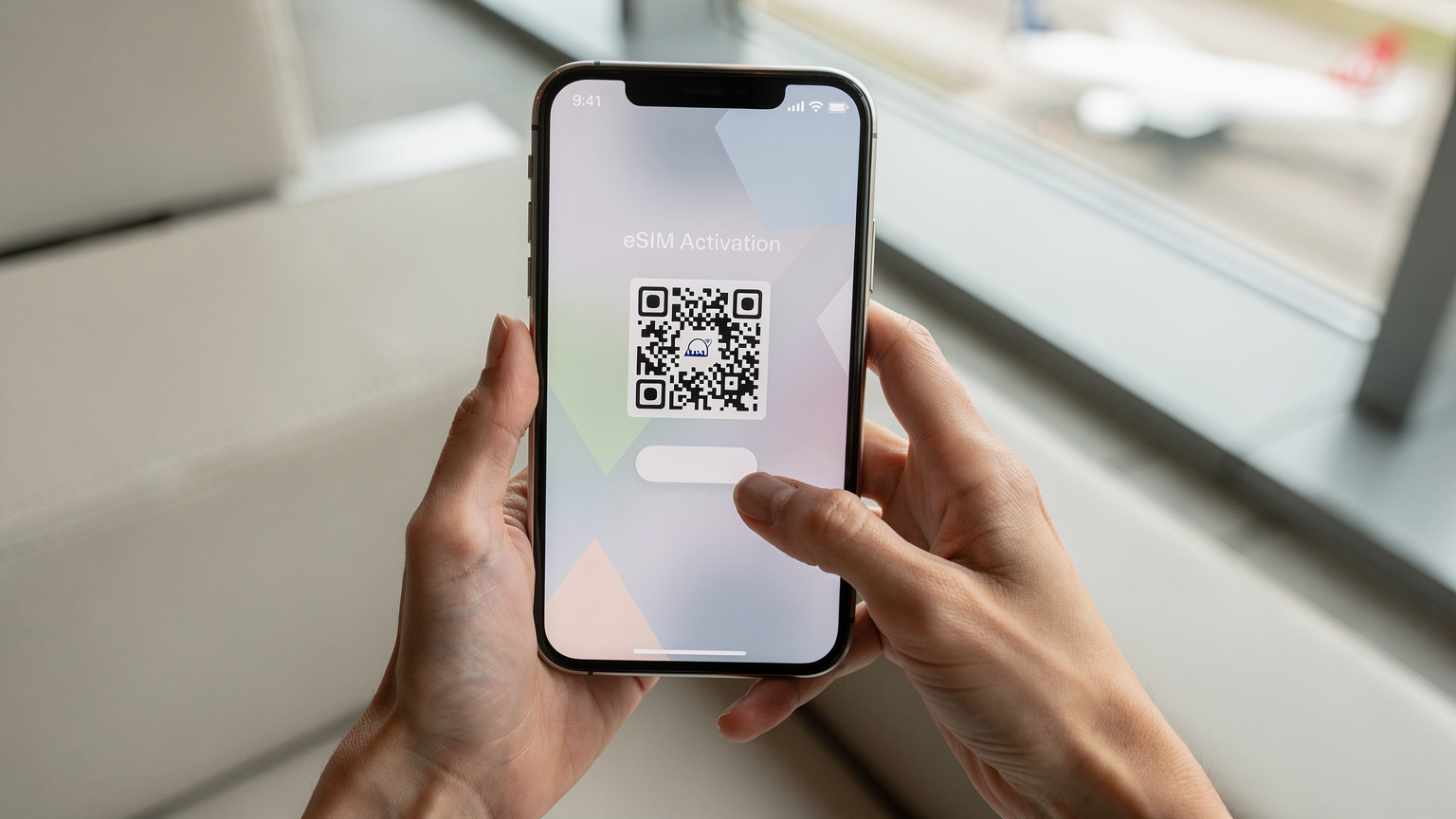 Des mains féminines tiennent un smartphone, l'écran affichant un QR code flou pour l'activation d'une eSIM, dans un environnement de voyage lumineux.