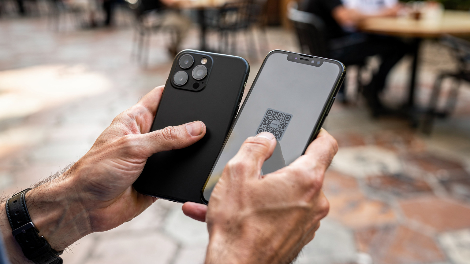 Крупна снимка на ръце, които държат смартфон и сканират QR код, вероятно за активиране на eSIM, с разфокусиран фон на туристически обект.