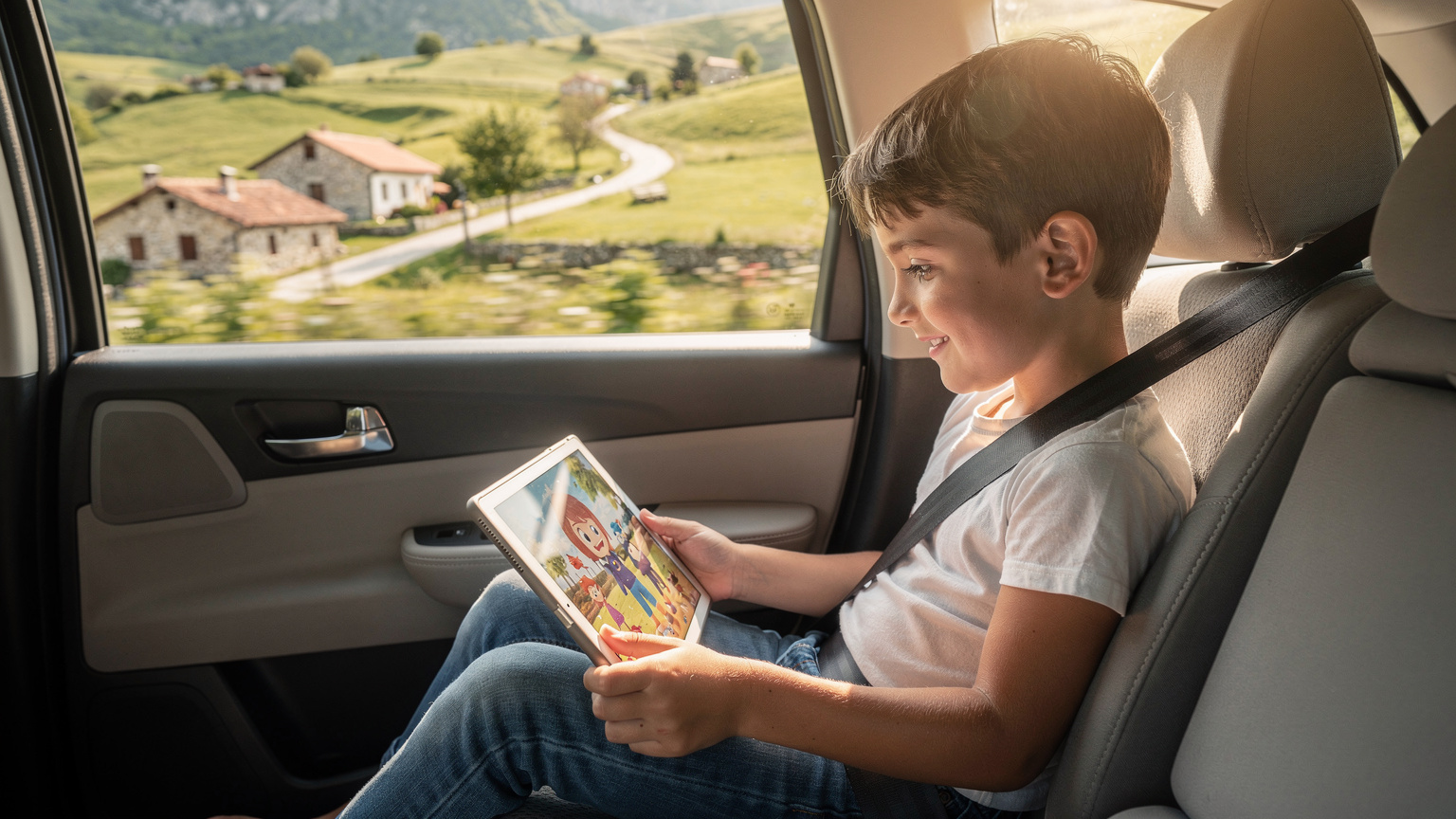 Ein lachendes Kind im Rücksitz eines fahrenden Autos, vertieft in ein Tablet, auf dem ein Animationsfilm läuft, während im Fenster die sonnige, hügelige Landschaft Albaniens vorbeizieht.
