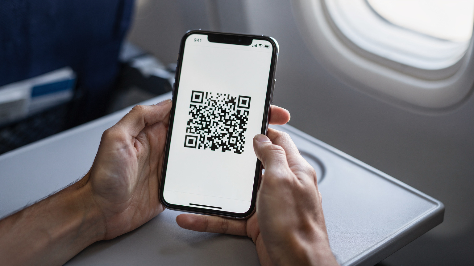 Manos de un viajero sosteniendo un smartphone, mostrando la pantalla con un código QR para activar la eSIM, en el cómodo asiento de un avión justo antes del despegue hacia Roma.