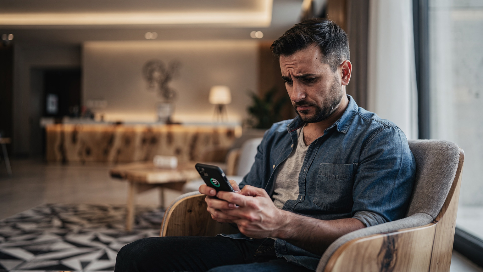 Ein Reisender sitzt nachdenklich in der Hotellobby in Tirana und blickt auf sein Smartphone, das eine Meldung über schlechten Empfang anzeigt.