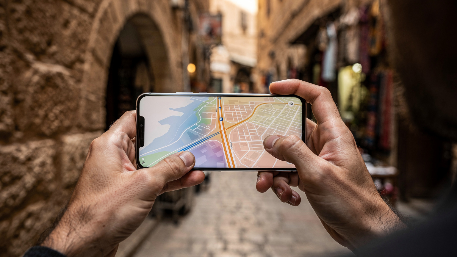 A close-up of a traveler's hands holding a smartphone, with a map app displaying a route through a historic Middle Eastern city, ancient architecture blurred in the background.