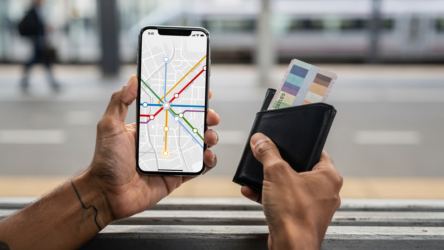 Manos de un viajero sosteniendo un teléfono con una aplicación de mapas abierta, mostrando la ruta de un metro, con un billete de transporte público asomando por una cartera de viaje.