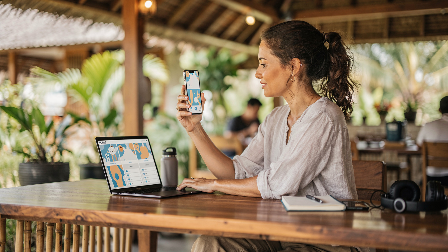 A digital nomad in a co-working space, holding up their phone, comparing data plans on Cellesim's website against a local carrier's pricing on another screen.