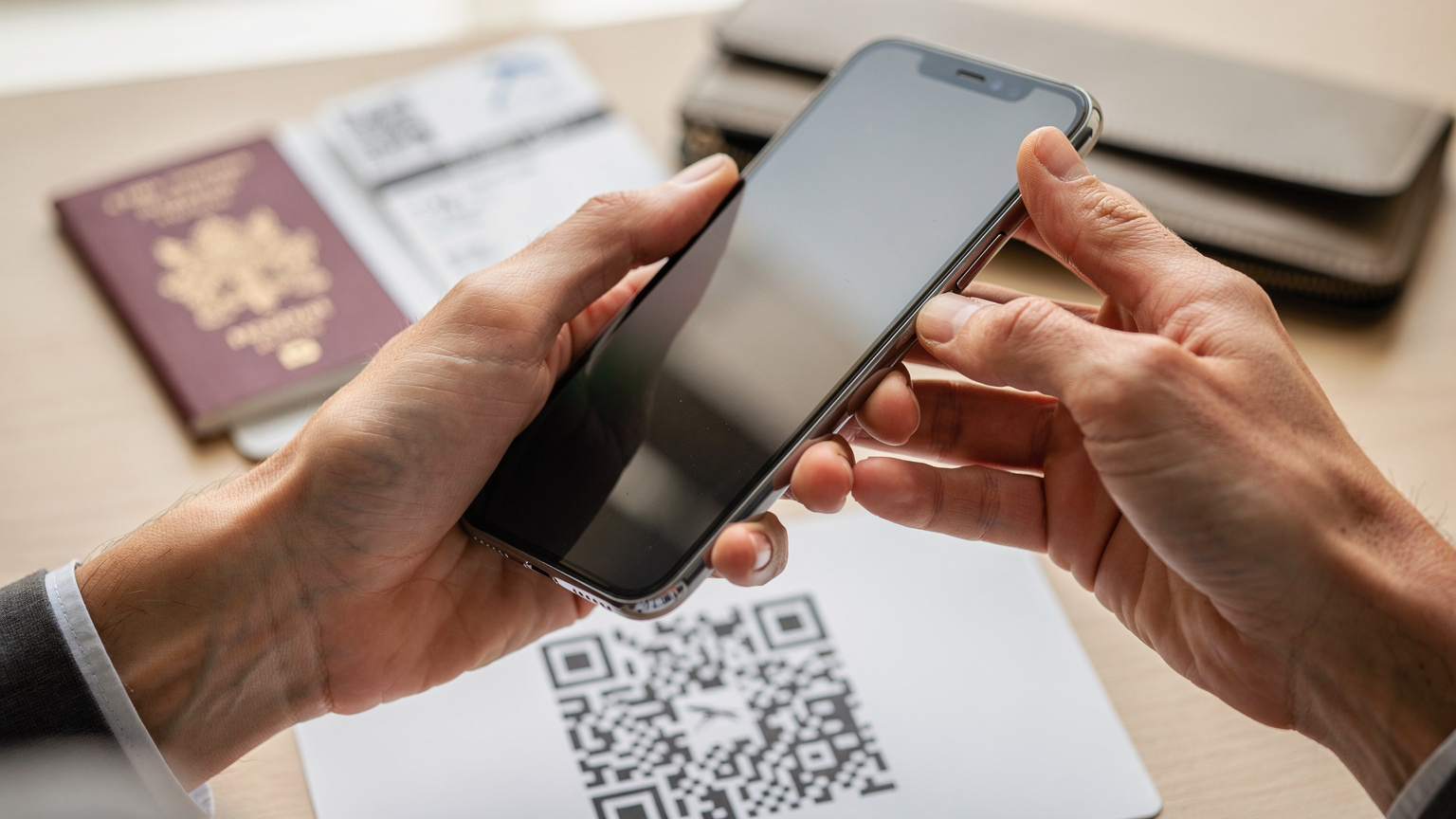 Gros plan sur des mains tenant un smartphone pour scanner un QR code d'eSIM, avec un passeport français et un billet d'avion floutés en arrière-plan, illustrant l'activation facile d'une eSIM voyage.